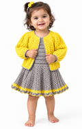 A toddler girl stands barefoot against a plain white studio background, wearing a bright yellow crocheted cardigan over a gray crocheted dress with a yellow and gray scalloped hem.