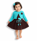 A toddler girl modeling a handmade crocheted dress set consisting of a turquoise blue cardigan and a matching headband, paired with a dark brown crocheted dress featuring a matching brown flower accent.