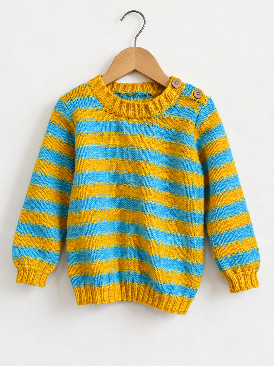 A children's knit sweater with horizontal yellow and light blue stripes, hanging on a wooden hanger against a plain white wall. The sweater has a crew neck, ribbed cuffs and hem, and two wooden buttons at the collar.